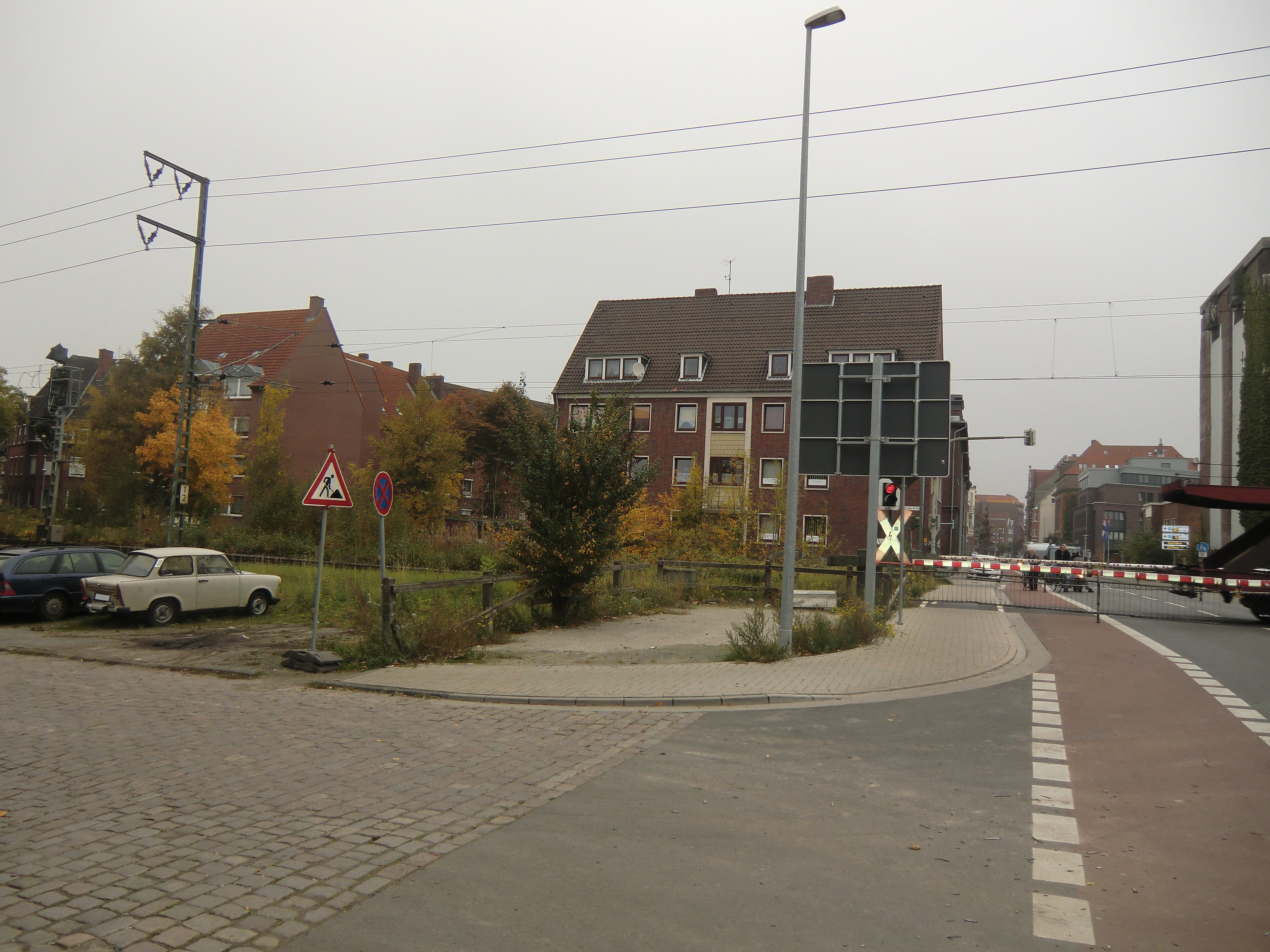 Farbfoto: Der Bahnübergang über die Nesserlander Straße in Emden bei geschlossener Eisenbahnschranke an der eingleisigen elektrifizierten Eisenbahnstrecke von Leer nach Emden. Vorne im Bild die Küstenbahnstraße. Rechts im Bild ein Autotransportwagen. Hinter der Schranke links die Fürbringerstraße. Im Oktober des Jahres 2010. Foto: Erwin Thomasius. 