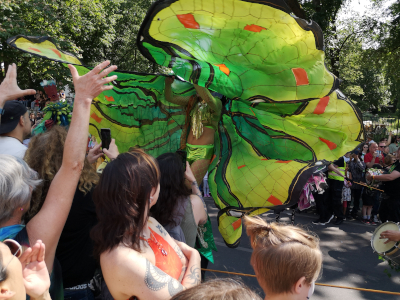 Farbfoto von als Schmetterling verkleideter Stelzenläuferin auf dem Umzug vom Karneval der Kulturen auf der Straße Hasenheide in Berlin am 28. Mai 2023. Fotograf: Erwin Thomasius.