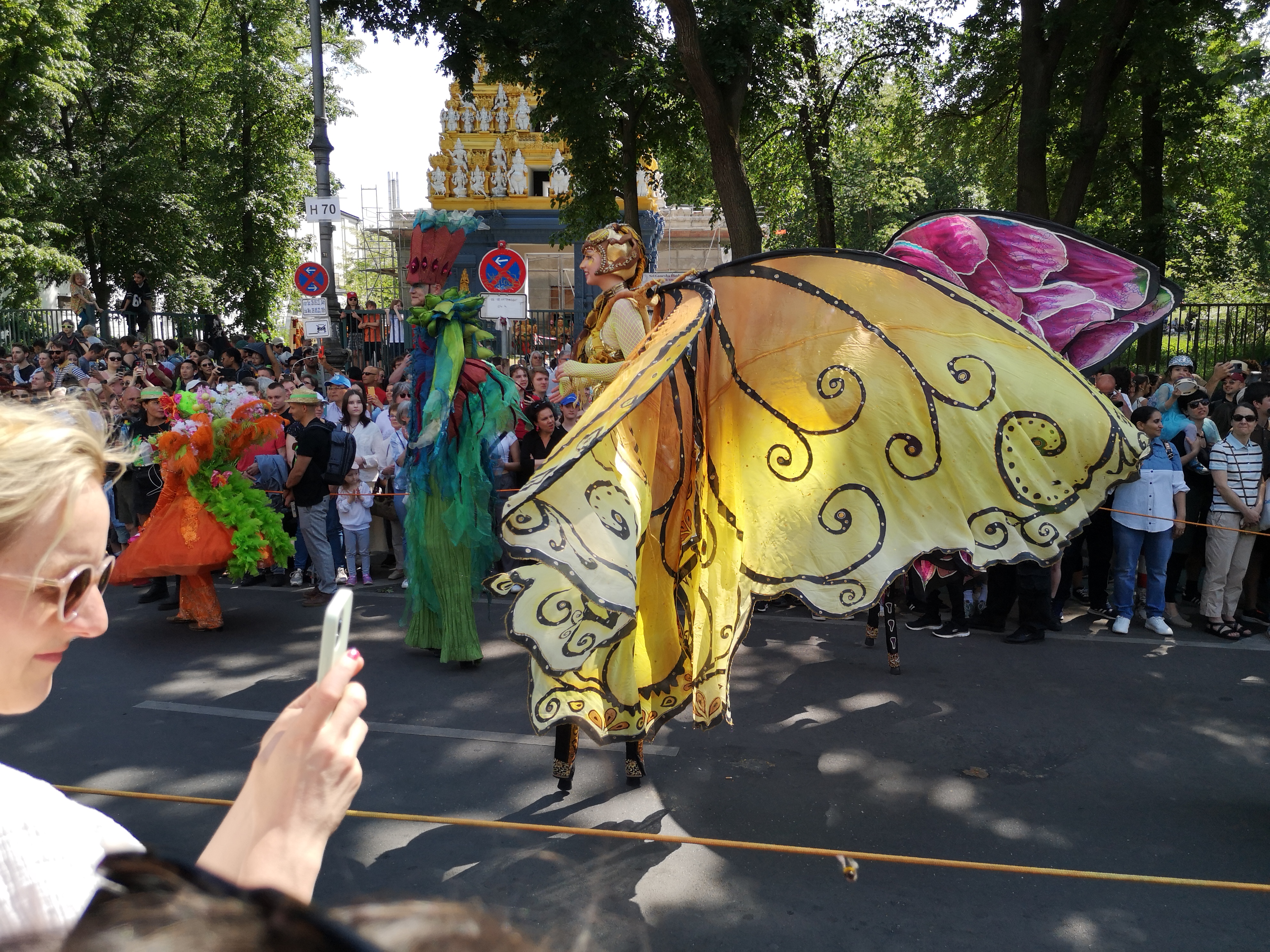 Foto von Stelzenläuferin im Schmetterlingskostüm beim Umzug vom Karneval der Kulturen am 28. Mai 2023 in Kreuzberg und in Neukölln in Berlin (Germany). Fotograf: Erwin Thomasius.