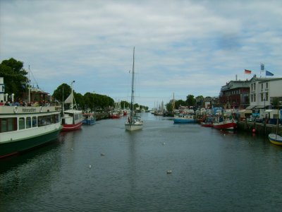 Farbphoto: Links das Hafenrundfahrtsschiff Käpp'n Brass, in der Mitte ein Segelboot und rechts im Bild der Fischhafen. In Warnemünde im Juni 2009. Photograph: Bernd Paepcke.