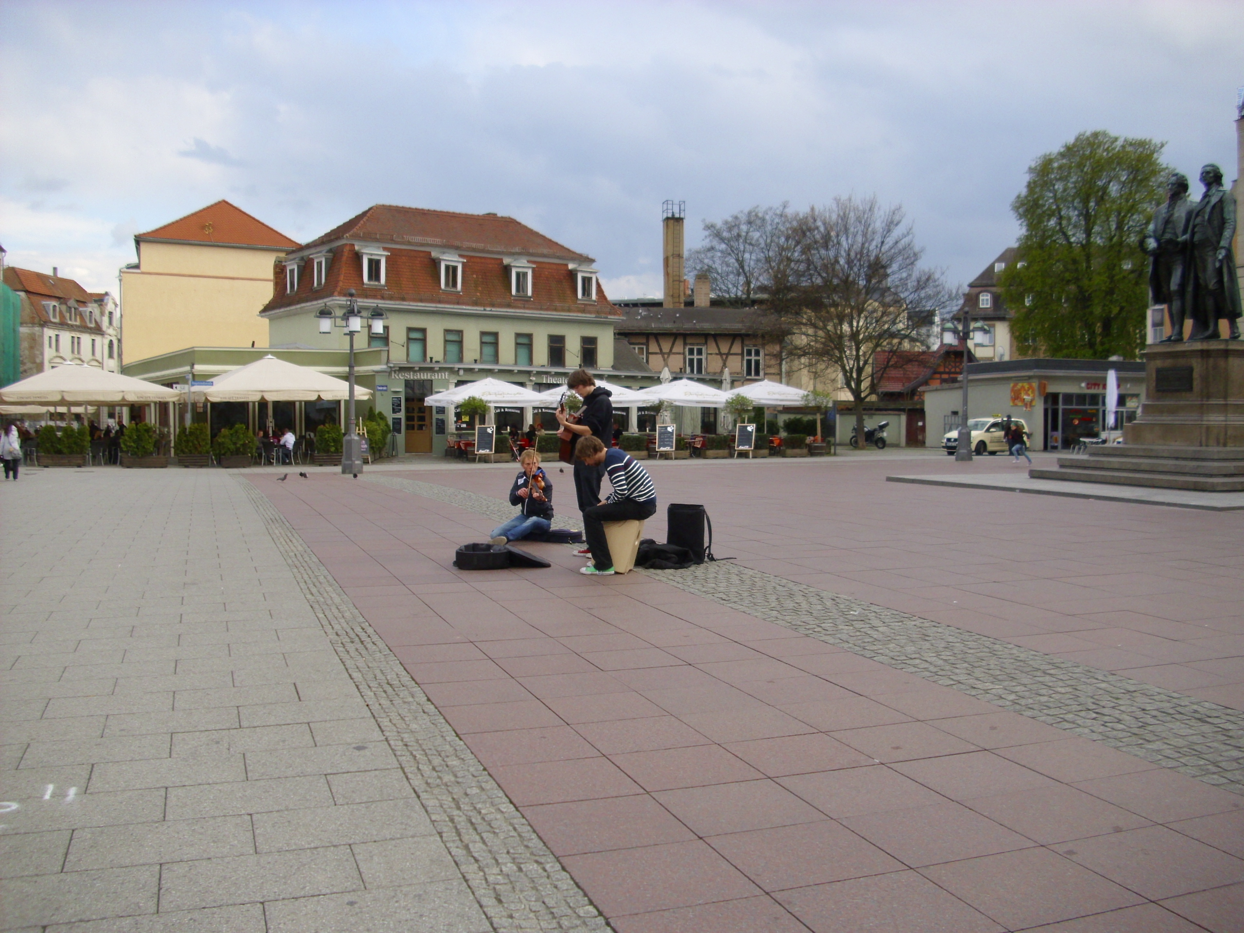 Farbfoto:  Junge Straßenmusikanten vor dem Goethe und Schiller Denkmal auf dem Theaterplatz in Weimar am Sonntag, dem 22. April im Jahre 2012. Fotograf: Bernd Paepcke.